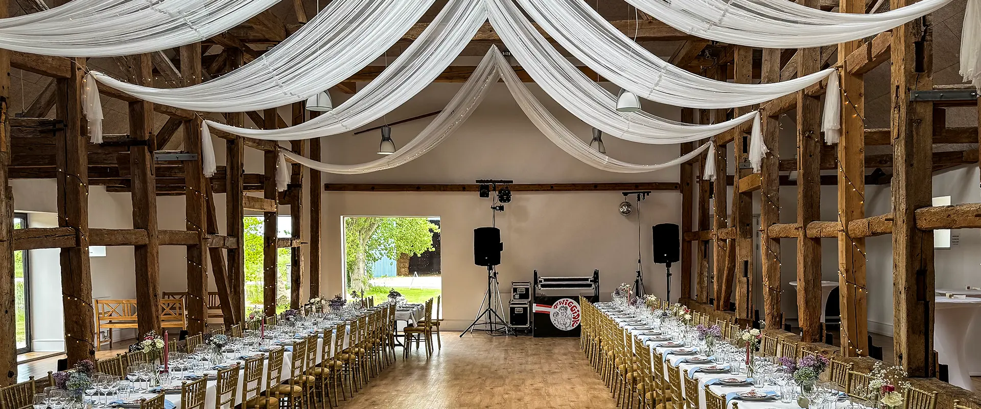 Erfaren bryllups-DJ fra Twiggi.dk spiller festmusik ved et elegant bryllupsarrangement. DJ’en står bag mixerpulten med professionelt udstyr, mens stemningsfuld LED-belysning oplyser dansegulvet, hvor glade gæster danser. Med over 50 års erfaring skaber Twiggi den perfekte musikalske ramme til bryllupsfester, hvor både brudevalsen og de nyeste hits får alle generationer på dansegulvet.